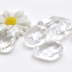 Puede incluir: Una margarita blanca con un centro amarillo y cuentas de cristal facetadas transparentes.