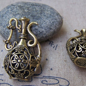 Puede incluir: Dos abalorios decorativos de metal dorado en forma de jarrones ornamentados y detallados. Los jarrones tienen un diseño floral y miden aproximadamente 5 cm de alto.