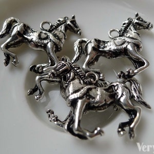 May include: Three silver-colored horse charms in various poses, each with a loop for attaching to jewelry or crafts. The horses are detailed with manes, tails, and harnesses, and are displayed on a white surface.