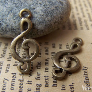 May include: Two antique gold-tone treble clef charms. The charms are on a textured, brown surface.