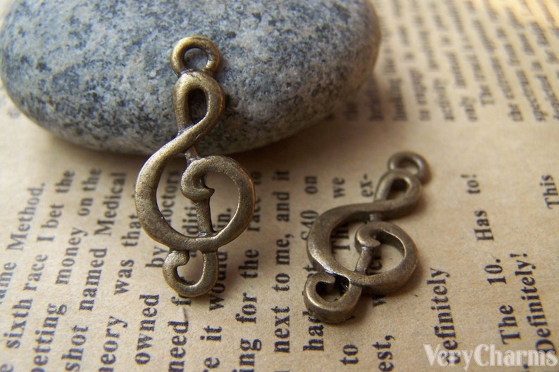 May include: Two antique gold-tone treble clef charms. The charms are on a textured, brown surface.