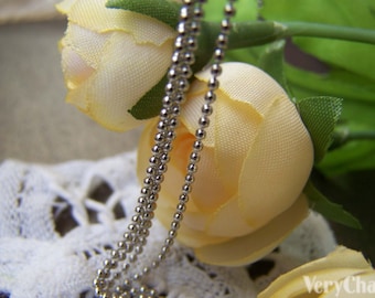 May include: A silver chain necklace with a ball chain design. The chain is laying on top of two cream-colored fabric roses.