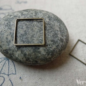 Può includere: Due cornici per foto quadrate in metallo color oro antico su uno sfondo di pietra grigia e tessuto bianco.