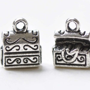 May include: Two silver-toned metal charms shaped like treasure chests with ornate details. The charms have a loop at the top for attaching to a necklace or bracelet.