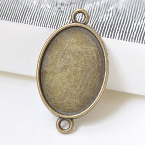 May include: Oval antique bronze bezel pendant with two loops for attaching to a chain or other jewelry components. The pendant has a textured surface and is designed for crafting.