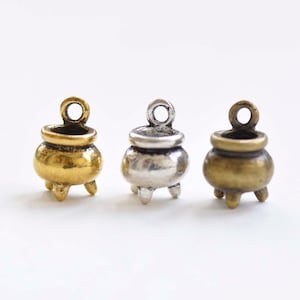 May include: Three miniature cauldron charms in gold, silver, and bronze finishes. Each charm has a loop at the top for hanging and three small feet.