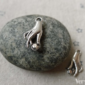 May include: Silver charm featuring a hand holding a small sphere. The charm is designed to be used for jewelry making.