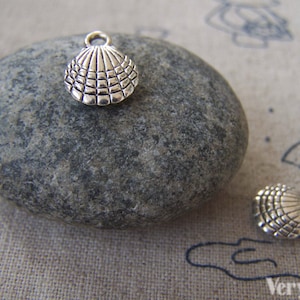 May include: Two silver-toned metal seashell charms with a detailed textured design. The charms have a loop at the top for attaching to jewelry or other crafts.