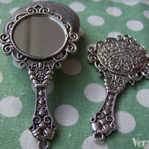 Peut inclure: Deux miroirs de poche argentés avec des motifs ornés. Le plus grand miroir a une surface réfléchissante ronde et une poignée décorative. Le plus petit miroir a un design circulaire et une boucle en bas.