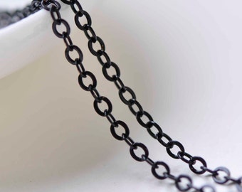 May include: Two strands of black chain, made of small, linked oval shapes. The chain is lying on a white surface.