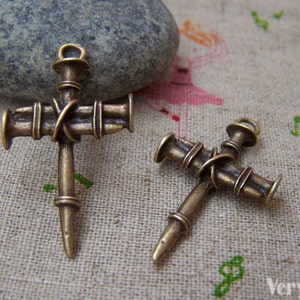 May include: Two antique gold-toned metal cross charms with nail heads. The larger cross is about 5 cm long and the smaller cross is about 3.8 cm long.