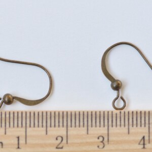 May include: Two bronze-colored earring hooks with a small loop at the end. The hooks are about 2 cm long and are shown next to a ruler.
