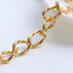 May include: A close-up of a gold chain necklace with a twisted link design. The chain is lying on a white surface.