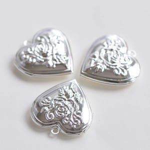 Puede incluir: Tres dijes de locket en forma de corazón plateados con un diseño floral.