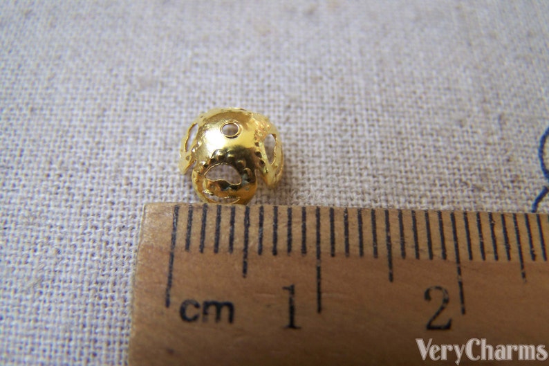 May include: Gold metal bead with a decorative openwork design. The bead is approximately 1 cm in diameter and has a hole for threading.