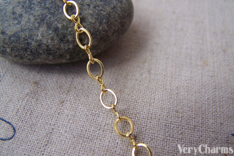 May include: A close-up of a gold chain with oval links. The chain is lying on a beige fabric surface.