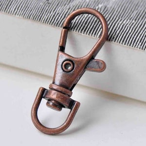 May include: A copper-coloured metal swivel clasp with a spring-loaded gate. The clasp is designed for attaching to keychains, bags, or other items.