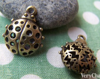 May include: Two antique gold-toned metal ladybug charms with intricate cut-out designs. One charm features a circle pattern, while the other has a starburst pattern.
