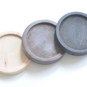 Puede incluir: Tres bases redondas de madera en diferentes colores: madera natural, marrón y negro. Las bases tienen un borde elevado y un pequeño agujero en el centro.