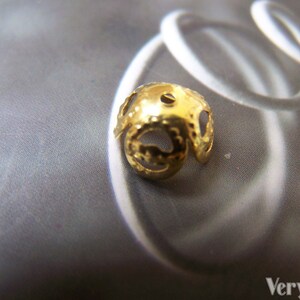 May include: Gold-toned metal bead with a decorative, openwork design. The bead has a round shape and a small hole in the center.