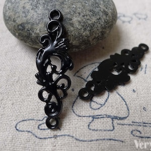 Puede incluir: Dos abalorios decorativos de metal negro con intrincados diseños florales. Los abalorios tienen dos agujeros para sujetarlos a joyas u otras manualidades.