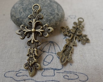 May include: Two ornate bronze cross charms with intricate floral designs. The crosses have a loop at the top for hanging.