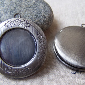 Può includere: Due ciondoli in argento, uno con un designo floreale e l'altro con una superficie liscia. Entrambi i ciondoli hanno un anello per attaccare una catena.