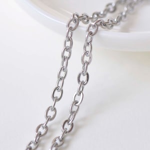 May include: Two silver chains lay on a white surface. The chains are made of oval links.