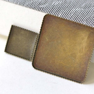 May include: Two square metal picture frames with a scalloped edge. The larger frame is brass colored and the smaller frame is a darker bronze color.