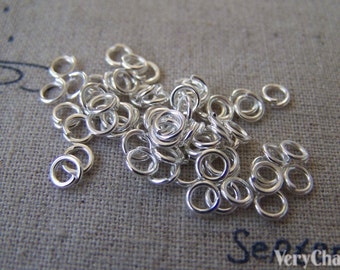 May include: A pile of silver jump rings, a type of jewelry finding used for connecting chains, cords, and other jewelry components.