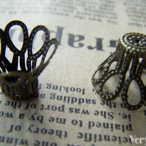 May include: Two antique gold-toned metal decorative embellishments with a scalloped design. The embellishments have a textured surface and are perfect for adding a vintage touch to crafts and jewelry.