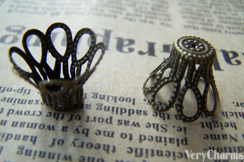 May include: Two antique gold-toned metal decorative embellishments with a scalloped design. The embellishments have a textured surface and are perfect for adding a vintage touch to crafts and jewelry.