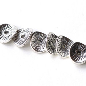 May include: Six silver-toned metal beads with a sunburst design and a hole in the centre. The beads are arranged in a row.