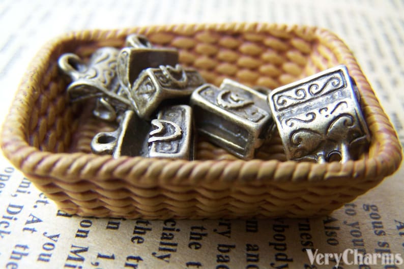 May include: A wicker basket filled with silver-toned metal charms. The charms are shaped like small boxes with intricate designs.