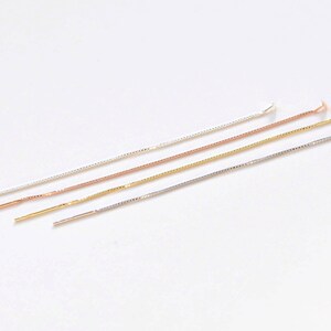May include: Four thin chains in silver, gold, and rose gold. The chains are laid out in a row on a white surface.