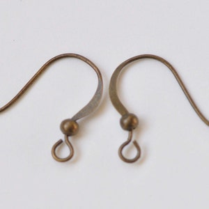 May include: Two bronze-colored earring hooks with a small ball at the top and a loop at the bottom.