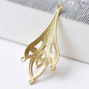 May include: Gold-toned metal pendant with a delicate, intricate design. The pendant has a teardrop shape with three loops at the bottom.
