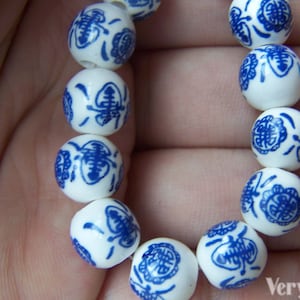 Puede incluir: Un brazalete blanco con cuentas de porcelana azul y blanca. Cada cuenta tiene un dise&ntilde;o floral azul. El brazalete est&aacute; en una mano.