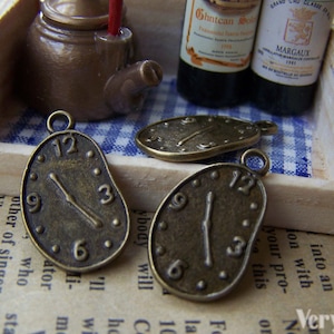 Puede incluir: Tres abalorios de reloj de bronce antiguo en forma de relojes derretidos. Los abalorios tienen marcas de números romanos y una sola aguja.