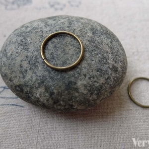 Puede incluir: Dos anillos de salto dorados, uno más grande que el otro, sobre una piedra gris. Los anillos son de metal y se utilizan para la fabricación de joyas.