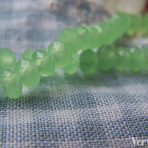 May include: A strand of light green glass beads, strung together to form a necklace or bracelet. The beads are faceted and have a translucent appearance.