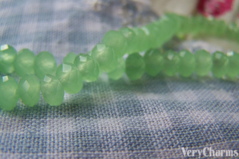 May include: A strand of light green glass beads, strung together to form a necklace or bracelet. The beads are faceted and have a translucent appearance.