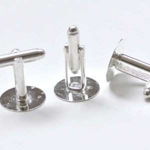 May include: Three silver cufflinks with a round base and a T-shaped bar. The cufflinks are made of metal and have a polished finish.