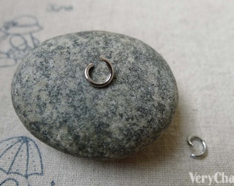 May include: Two silver jump rings, one on a gray rock and one on a white surface. The jump rings are used for jewelry making.