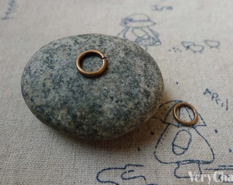 May include: Two small, round, copper jump rings on a gray stone and a white fabric background. The jump rings are about 1/2 inch in diameter.