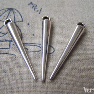 Peut inclure: Trois breloques en métal argenté en forme de cône avec une boucle en haut. Les breloques mesurent environ 5 cm de long.