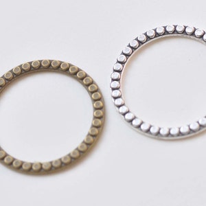 May include: Two metal rings with a beaded edge. The ring on the left is bronze and the ring on the right is silver.