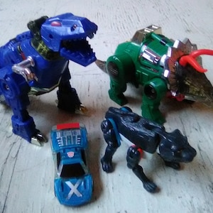 May include: Four toy robots in different dinosaur and animal forms. A blue Tyrannosaurus Rex, a green Triceratops, a black panther, and a blue car.