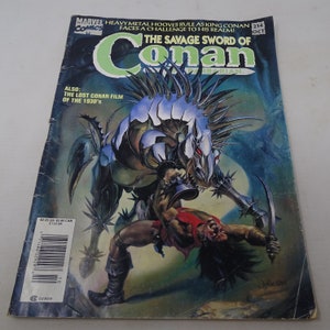 May include: A comic book cover featuring a muscular man fighting a monstrous creature with a sword. The cover is for the comic book "Conan the Barbarian" and the title "The Savage Sword of Conan" is printed in large letters. The issue number is 214 and the month is October.