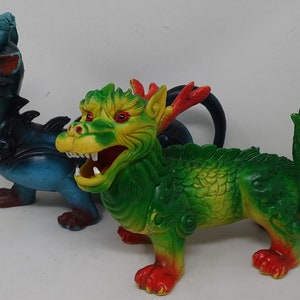 Può includere: Due draghi giocattolo di plastica. Uno è blu e nero con accenti rossi. L'altro è verde e giallo con accenti rossi.